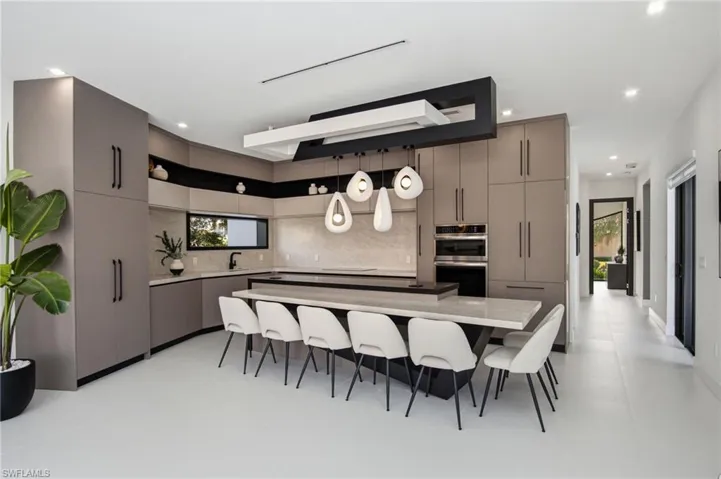 Modern kitchen featuring an expansive island with seating, integrated appliances, slab cabinetry, and a sleek linear lighting fixture