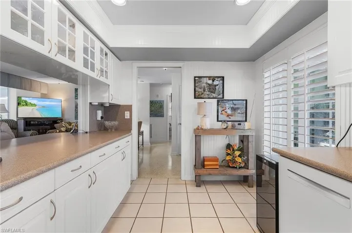 Kitchen featuring ornamental molding, white cabinetry, beverage cooler, and tasteful backsplash and Plantation Shutters on every window