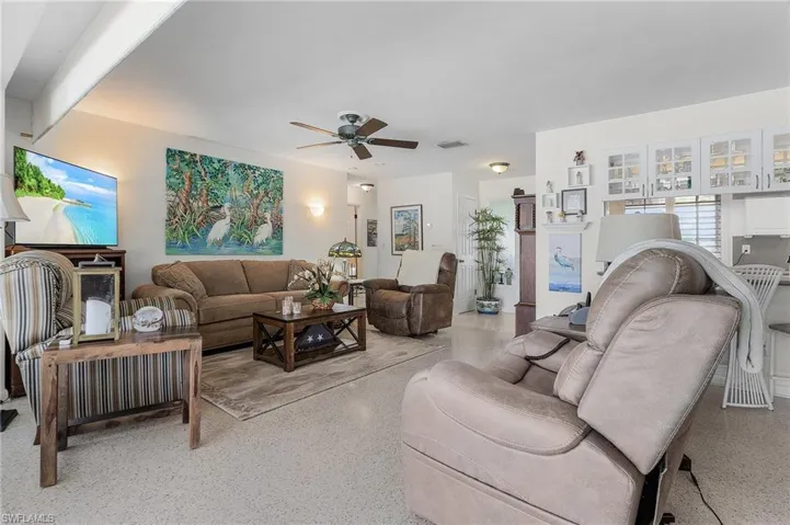 Living room featuring ceiling fan, terrazo floors and bar to kitchen with overhead glass door cabinets