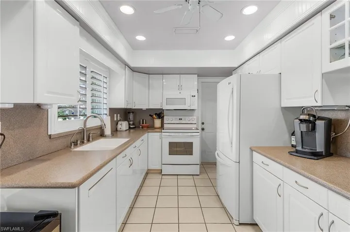Kitchen featuring white cabinets, sink, light tile patterned floors, and white appliances and corian counters and backsplash with pantry and door to garage