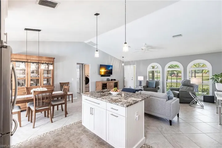 Kitchen featuring lofted ceiling, hanging light fixtures, stainless steel fridge, white cabinets, and light stone counters
