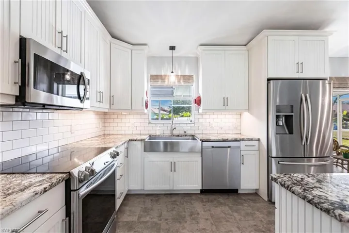 Kitchen with decorative backsplash, sink, white cabinets, decorative light fixtures, and appliances with stainless steel finishes