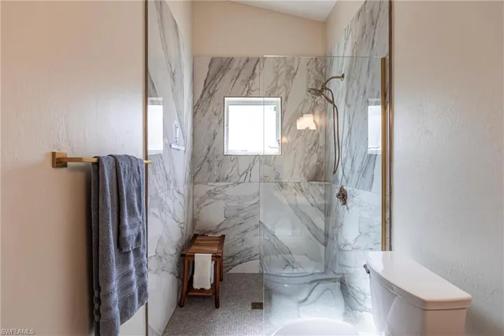 Primary Bathroom featuring toilet, vaulted ceiling, tile walls, and tiled shower