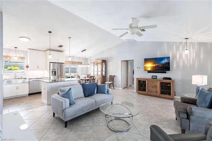 Living room with light tile patterned flooring, ceiling fan, sink, and vaulted ceiling