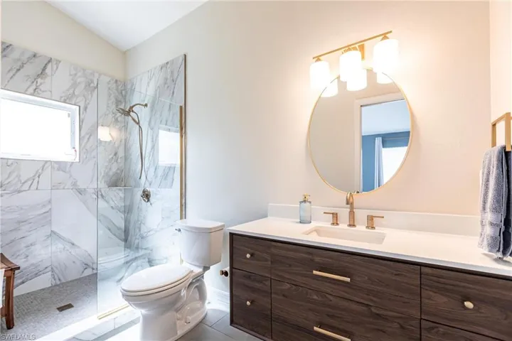 Primary Bathroom with tiled shower, toilet, tile patterned flooring, vaulted ceiling, and vanity