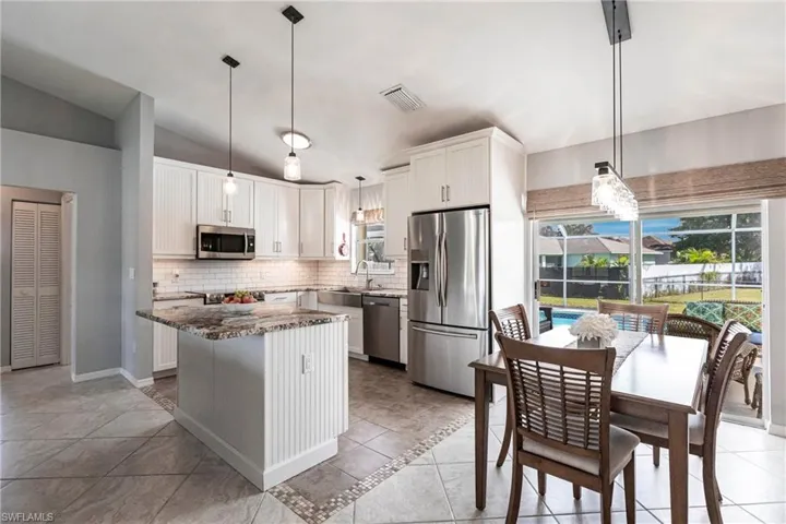 Kitchen featuring lofted ceiling, a kitchen island, stainless steel appliances, decorative light fixtures, and white cabinets