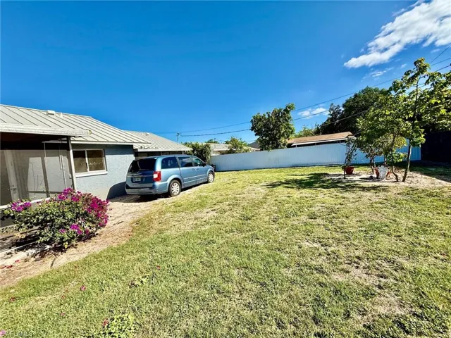 The property features a spacious yard with a lawn, a white privacy fence, and mature trees