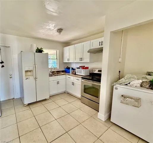 The kitchen features white cabinetry with dark hardware, a stainless steel range and hood, and a white side-by-side refrigerator