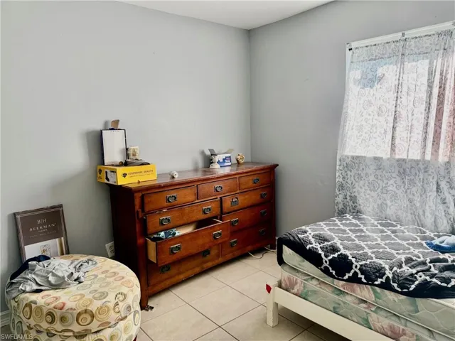 This room features neutral-toned walls, tile flooring, and a window with sheer patterned curtains