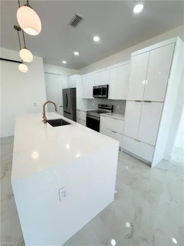 Kitchen with white cabinets, appliances with stainless steel finishes, pendant lighting, modern cabinets, and light marble finish floors