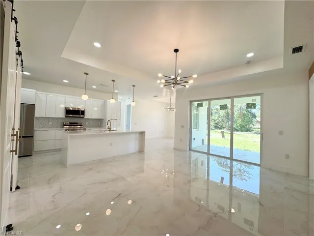 Kitchen with white cabinets, open floor plan, hanging light fixtures, a kitchen island with sink, and recessed lighting