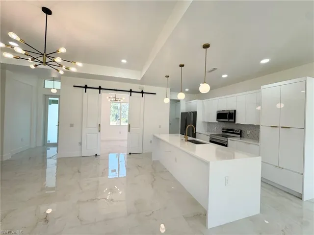 Kitchen featuring a barn door, modern cabinets, white cabinetry, pendant lighting, and appliances with stainless steel finishes