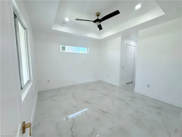Empty room with a tray ceiling, light marble finish floors, recessed lighting, and ceiling fan