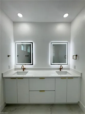 Bathroom with double vanity and light marble finish flooring