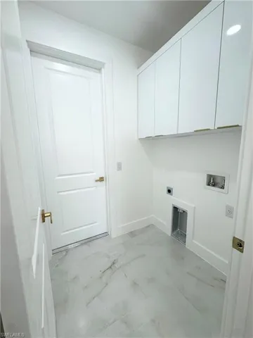 Laundry area with hookup for a washing machine, electric dryer hookup, light marble finish floors, and cabinet space