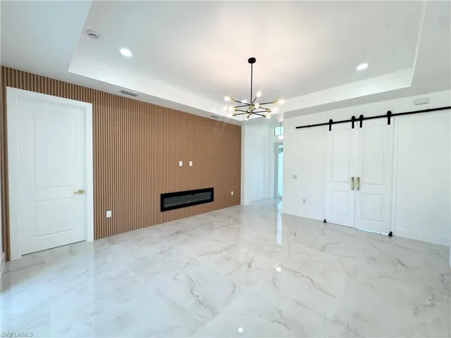 Unfurnished living room featuring a barn door, a raised ceiling, recessed lighting, wood walls, and a glass covered fireplace