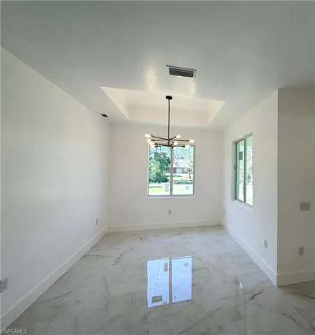 Unfurnished dining area featuring a tray ceiling, a chandelier, and light marble finish floors