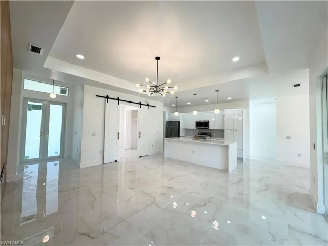 Unfurnished living room with a barn door, a tray ceiling, a chandelier, light marble finish flooring, and recessed lighting