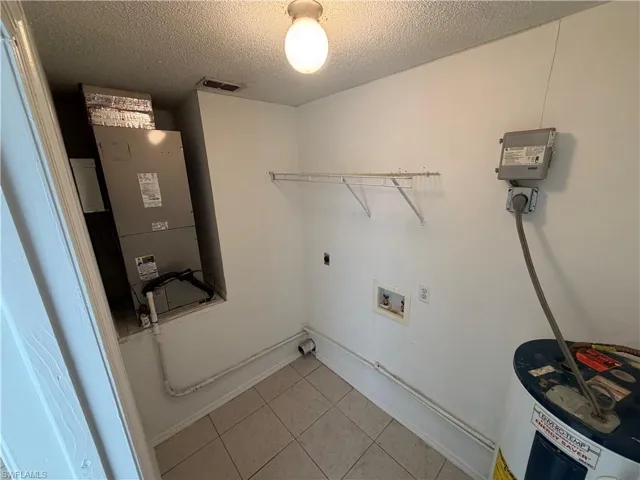 Laundry room featuring hookup for an electric dryer, water heater, a textured ceiling, heating unit, and light tile patterned floors