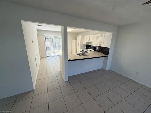 Kitchen featuring white cabinets, decorative backsplash, freestanding refrigerator, black electric range oven, and light tile patterned floors