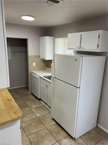 Kitchen with white cabinetry, fridge, a textured ceiling, dishwasher, and light tile patterned floors