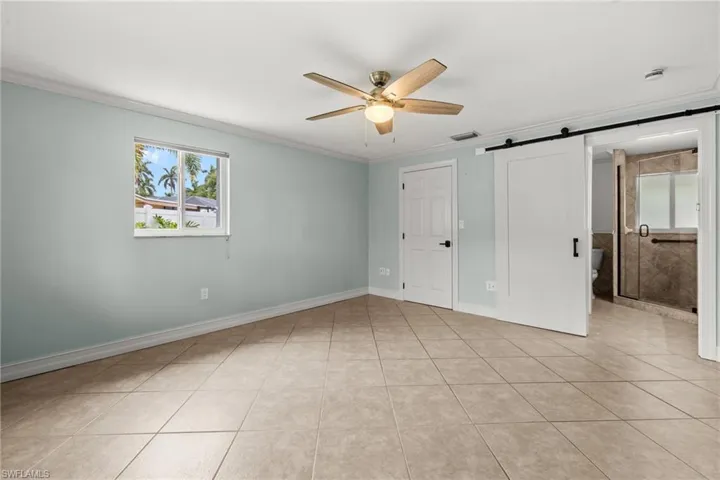 Unfurnished bedroom featuring multiple windows, crown molding, light tile patterned floors, a barn door, and ceiling fan