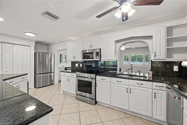 Kitchen featuring stainless steel appliances, a sink, a ceiling fan, arched walkways, and light tile patterned floors