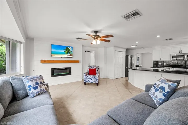 Living area featuring light tile patterned floors, a glass covered fireplace, a ceiling fan, recessed lighting, and baseboards