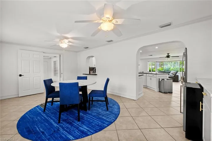Dining space featuring arched walkways, light tile patterned floors, ceiling fan, and crown molding