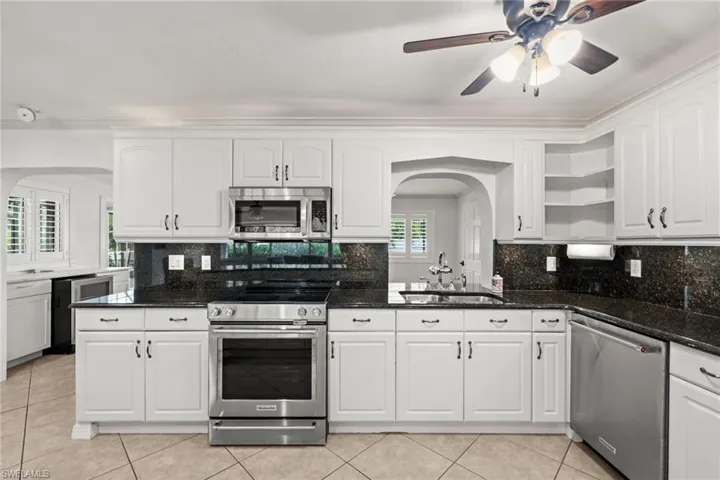 Kitchen featuring appliances with stainless steel finishes, open shelves, arched walkways, and white cabinetry