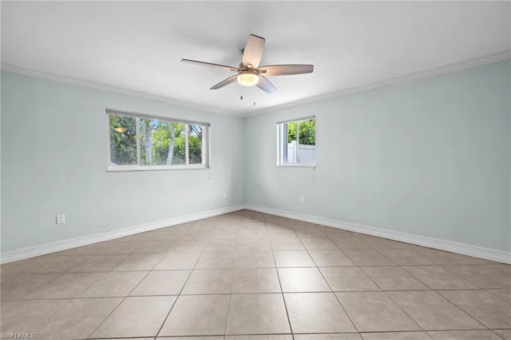 Unfurnished bedroom with ornamental molding, baseboards, ensuite bath, light tile patterned flooring, and ceiling fan