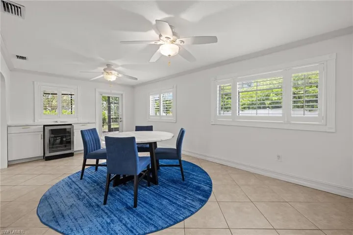 Dining area with wine cooler, light tile patterned flooring, crown molding, baseboards, and ceiling fan