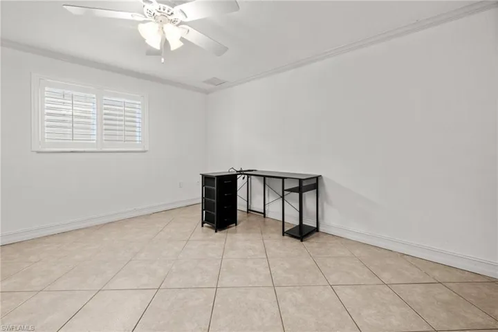 Empty room with ceiling fan, ornamental molding, light tile patterned floors, and baseboards