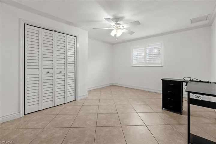 Unfurnished bedroom featuring crown molding, a closet, a ceiling fan, light tile patterned floors, and baseboards