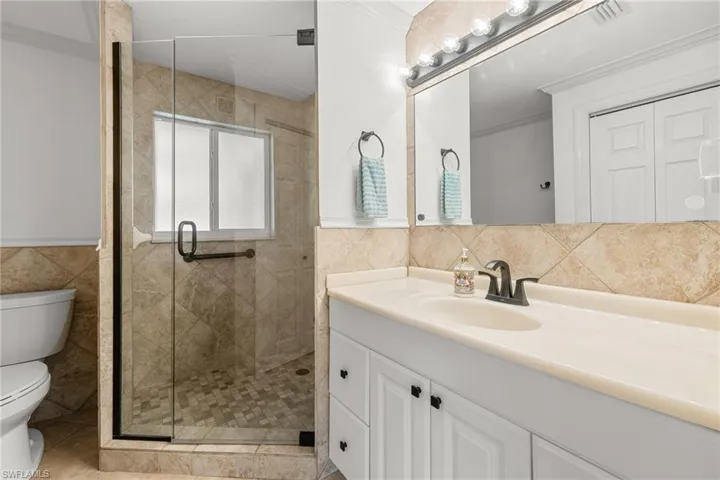 Bathroom with tile walls, toilet, a shower stall, vanity, and wainscoting
