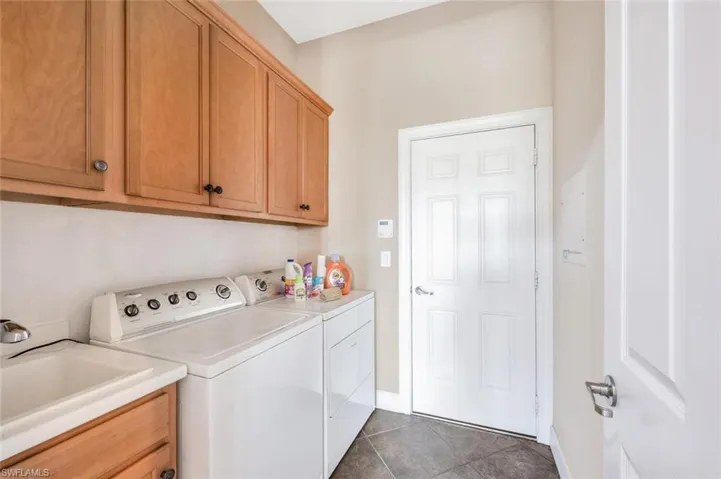 Laundry room with separate washer and dryer, cabinets, tile patterned flooring, and sink