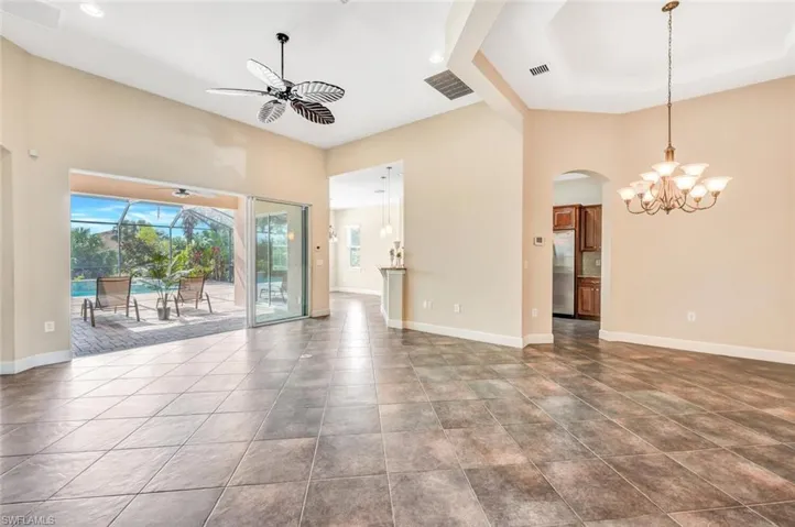 Unfurnished living room featuring tile patterned flooring, ceiling fan with notable chandelier, and a towering ceiling