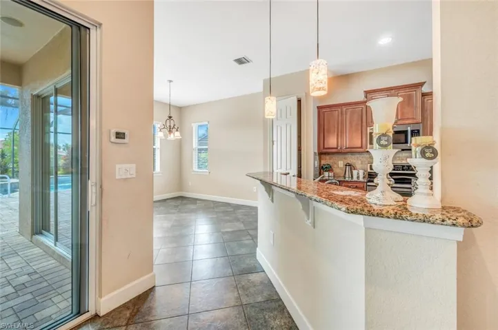 Kitchen featuring backsplash, appliances with stainless steel finishes, dark tile patterned flooring, pendant lighting, and a kitchen breakfast bar
