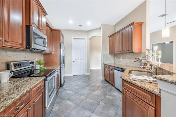 Kitchen with appliances with stainless steel finishes, sink, tile patterned flooring, hanging light fixtures, and decorative backsplash