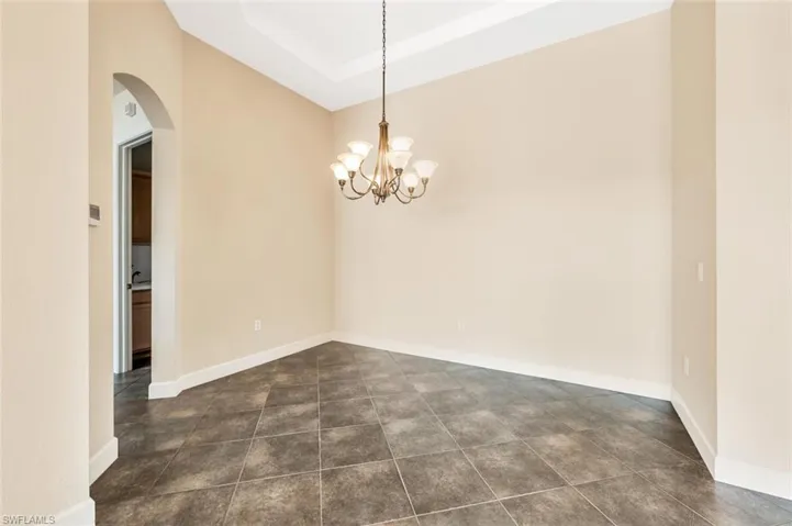 Tiled spare room featuring an inviting chandelier and a raised ceiling