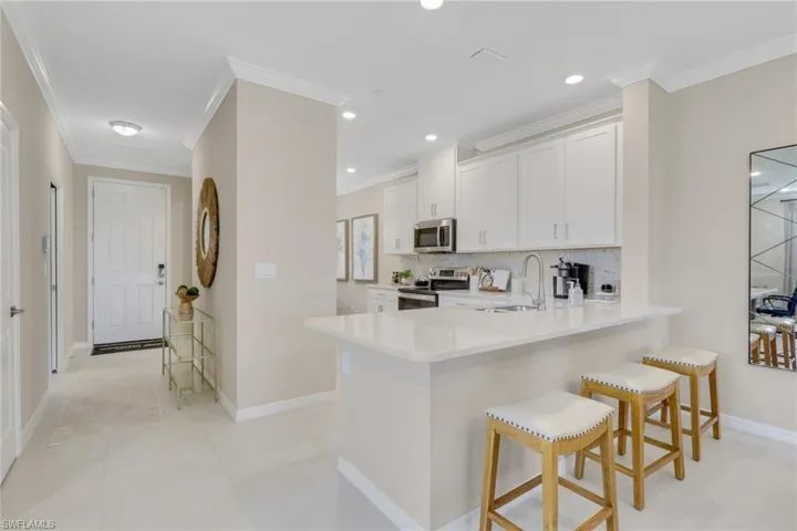 Kitchen with ornamental molding, tasteful backsplash, white cabinetry, stainless steel appliances, and a kitchen breakfast bar