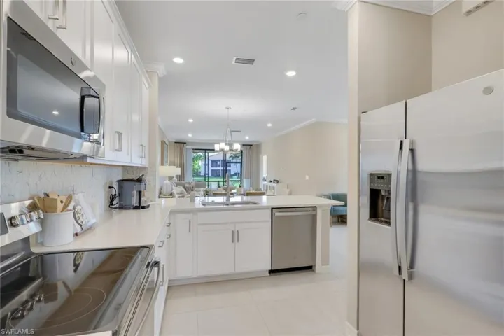 Kitchen featuring appliances with stainless steel finishes, ornamental molding, white cabinets, decorative backsplash, and pendant lighting