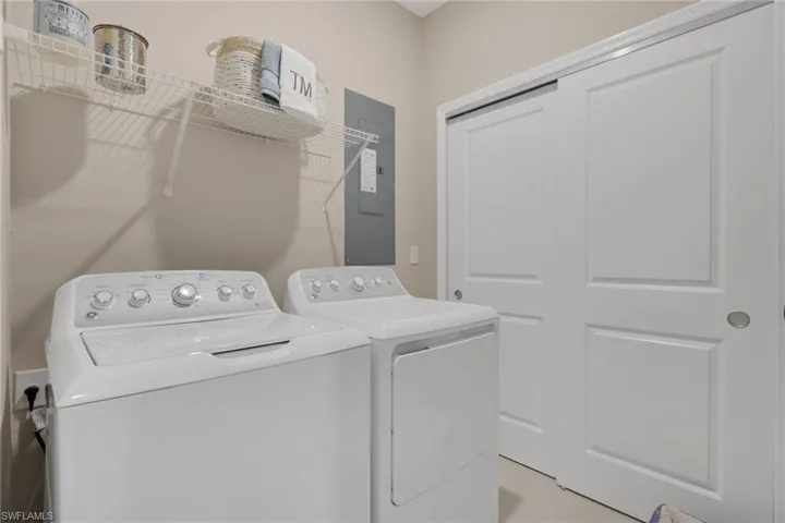 Laundry area with electric panel, light tile patterned flooring, and washing machine and dryer