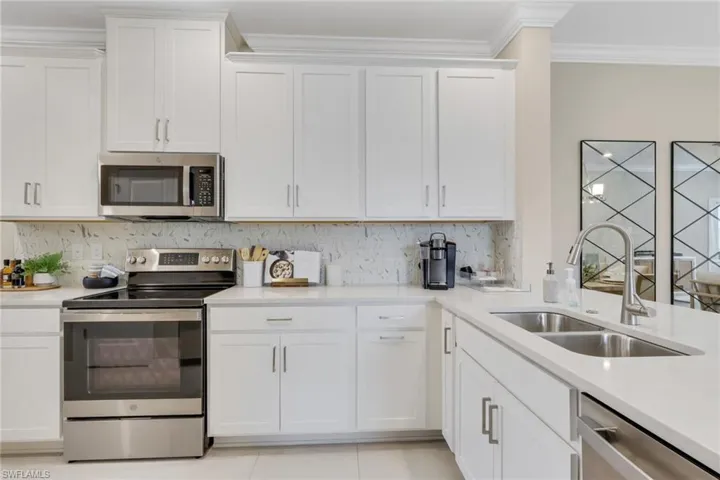 Kitchen with stainless steel appliances, white cabinetry, light tile patterned floors, and crown molding