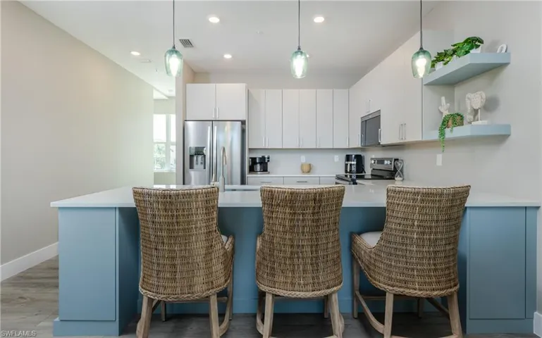 2nd-level kitchen featuring a light blue island with counter seating, stainless steel appliances, white cabinetry, and recessed lighting