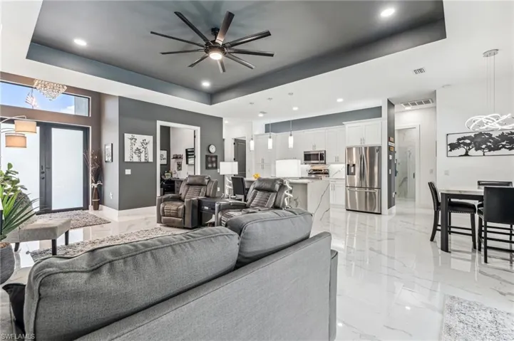 Living area featuring marble finish floor, visible vents, ceiling fan with notable chandelier, and a raised ceiling