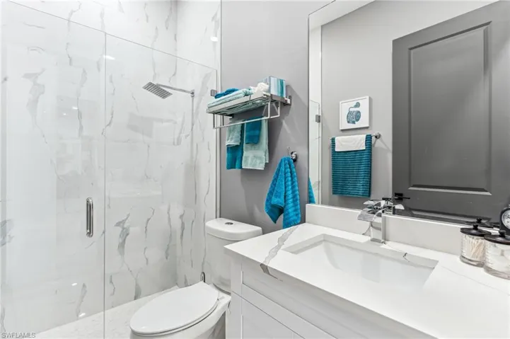 Bathroom featuring toilet, vanity, and a marble finish shower