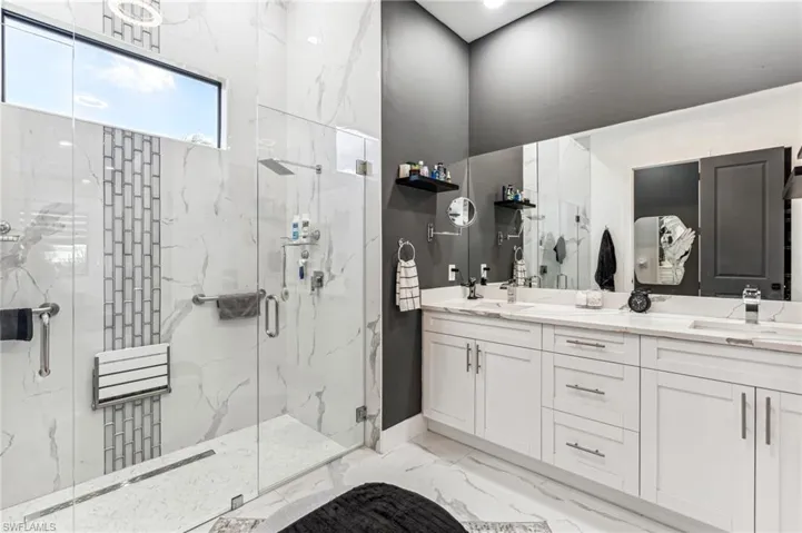 Bathroom featuring a marble finish shower, marble finish floor, a sink, and double vanity