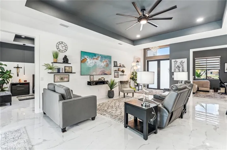 Living area with marble finish floor, a tray ceiling, visible vents, and ceiling fan