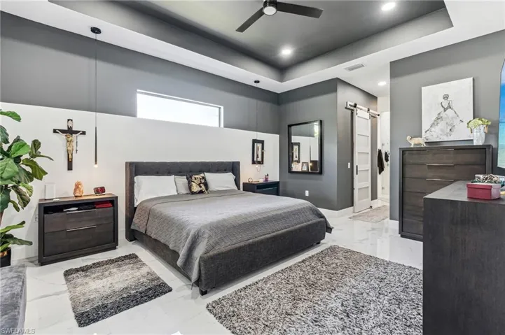 Bedroom with a barn door, visible vents, marble finish floor, and a raised ceiling